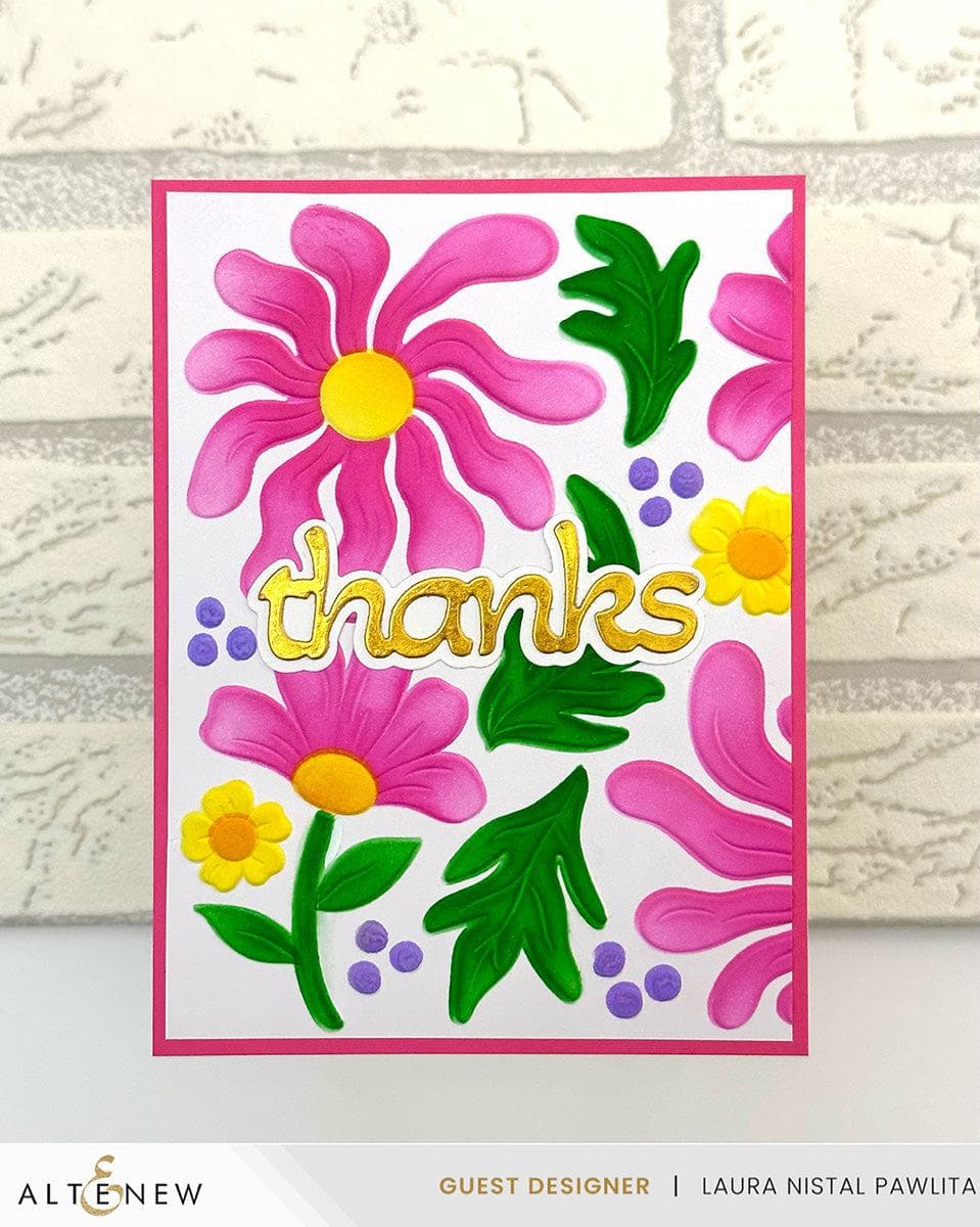 A handmade greeting card with a white background, featuring colorful pink and yellow flowers, green leaves, purple berries, and the word 'thanks' in gold foil. The card is displayed against a light gray brick-patterned background.