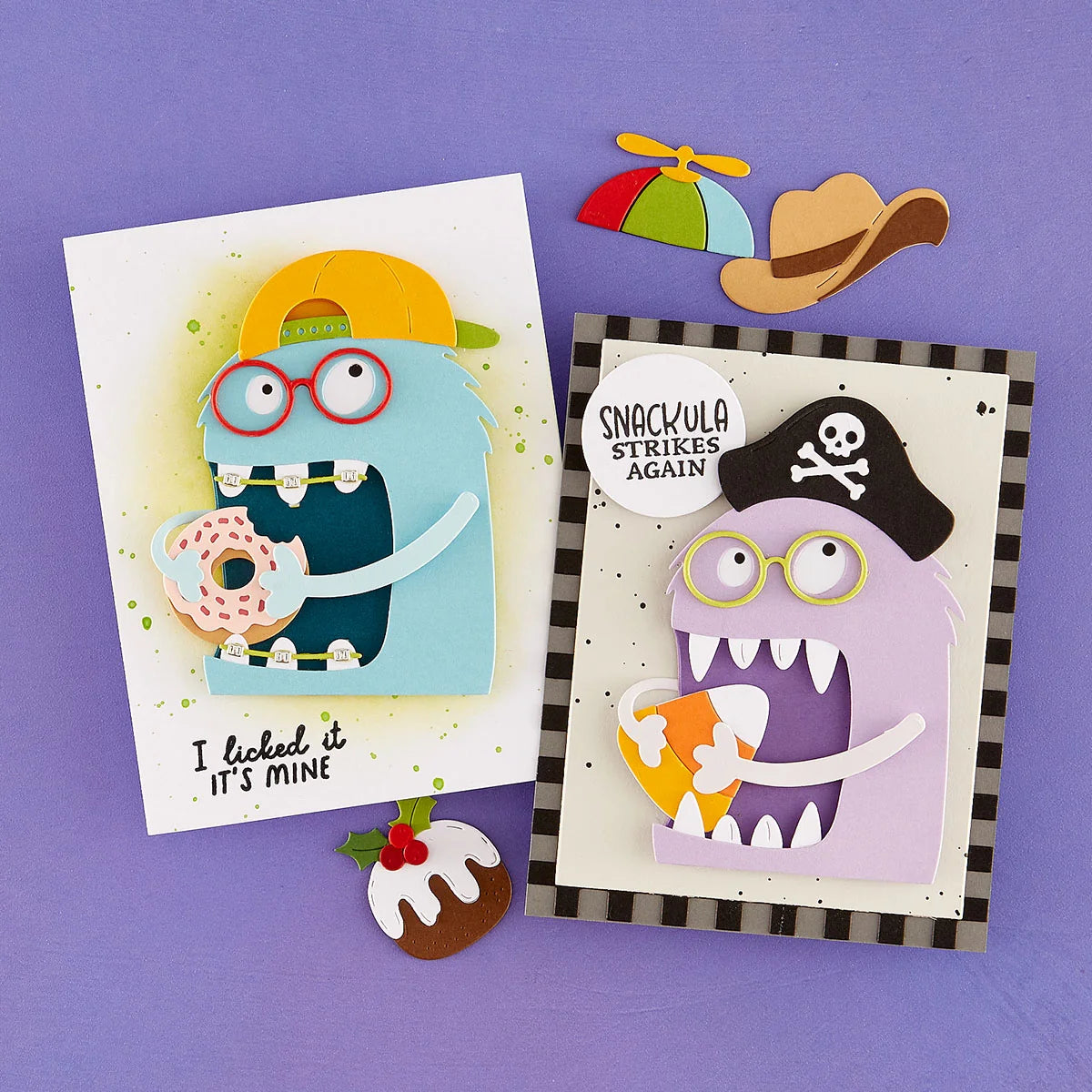 Two handmade layered paper cards displayed on a purple background, each featuring a cartoon monster with glasses and a speech bubble. One card shows a blue monster eating a donut and reads 'I licked it IT'S MINE.