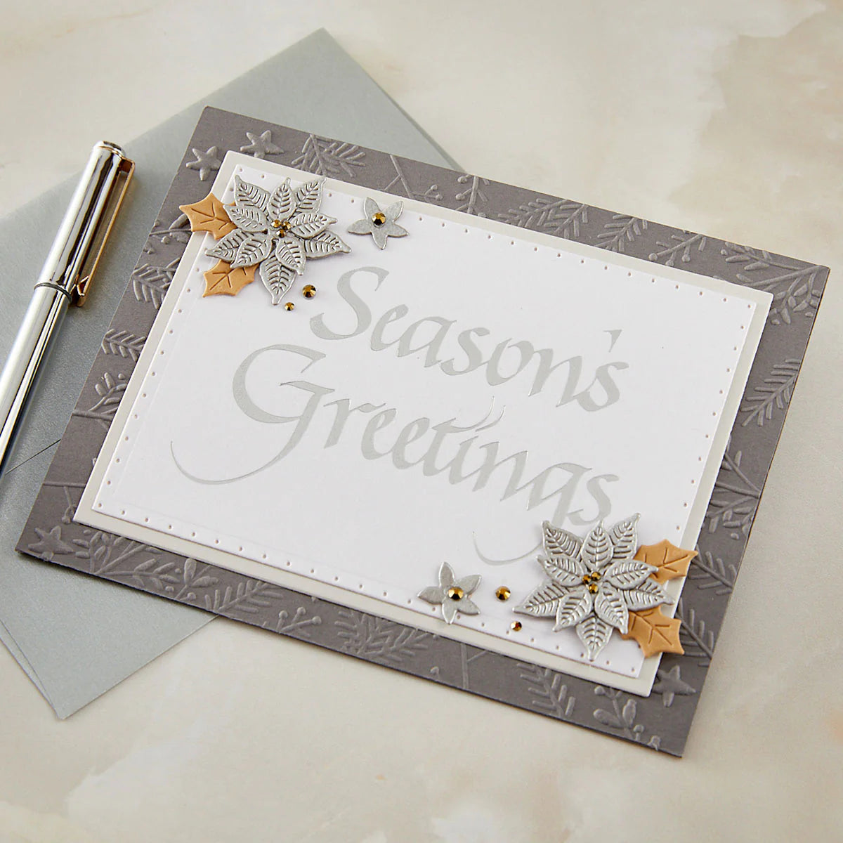 Season's Greetings card with silver poinsettia dies on embossed gray cardstock