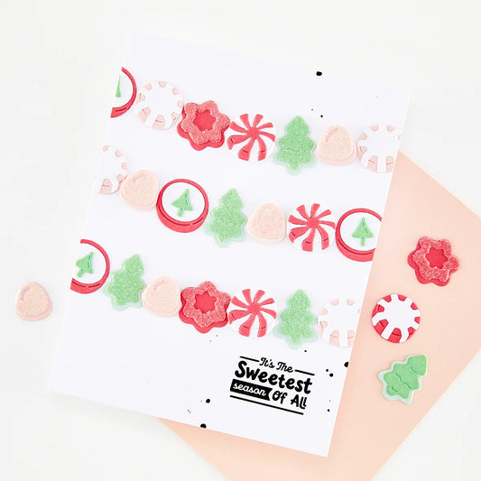 A white greeting card with a festive Christmas garland design made of red, pink, and green die-cut stickers, placed on top of a peach envelope. The card features the text 'It's The Sweetest season of all' at the bottom.