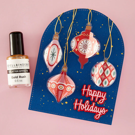 Spellbinders blue arched card with red sticker ornaments and gold splatter with happy holidays pink sentiment on red shadow.