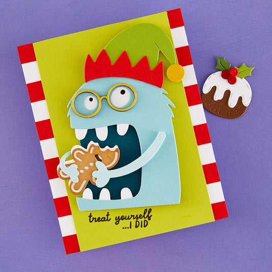 A handmade layered paper card featuring a light blue monster wearing a red and green elf hat and glasses, holding a gingerbread cookie. The card has a red and white striped border, the text 'treat yourself .