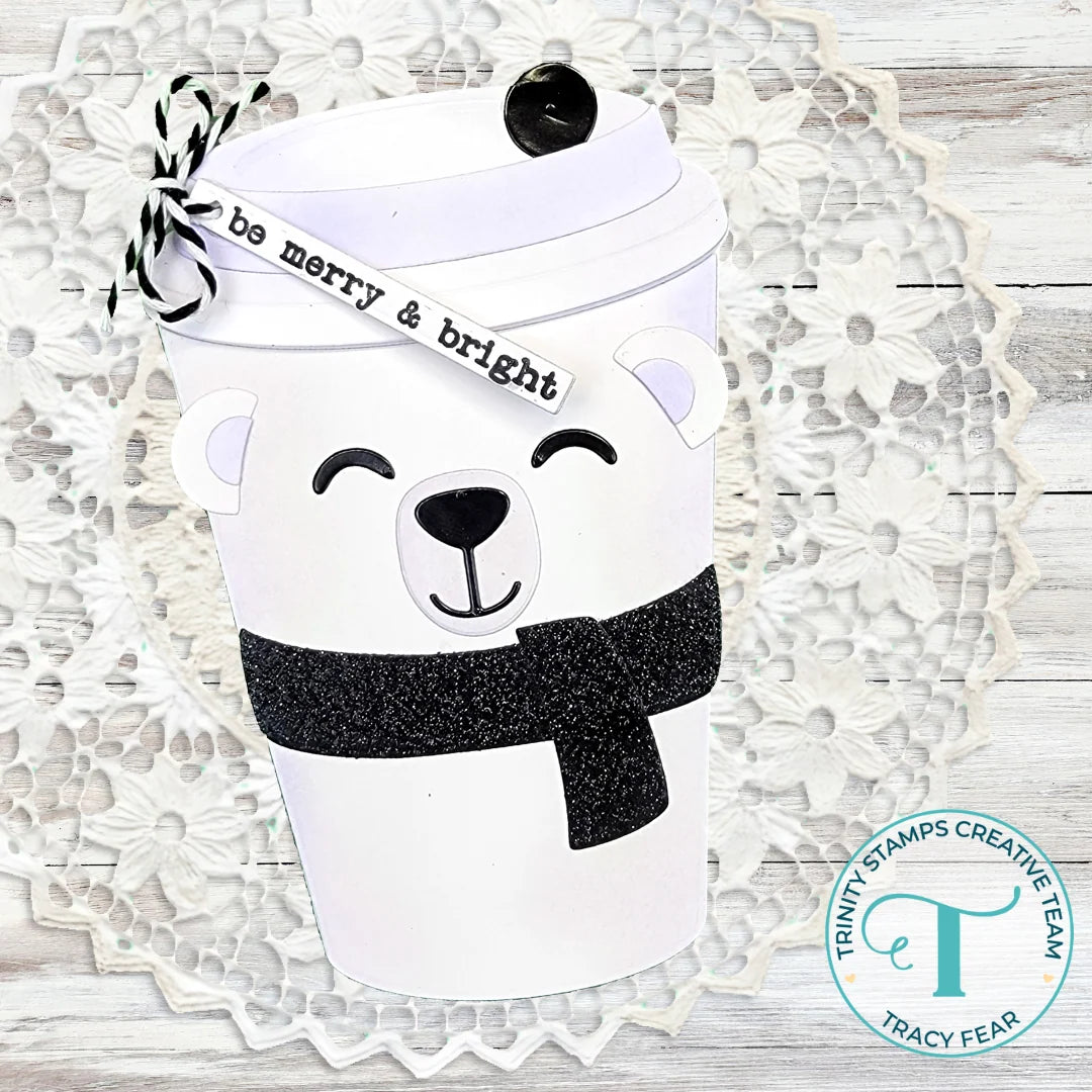 white shaped hot cup card with a white polar bear and black glitter scarf on a doily on woodedn backgroung with Trinity stamps logo