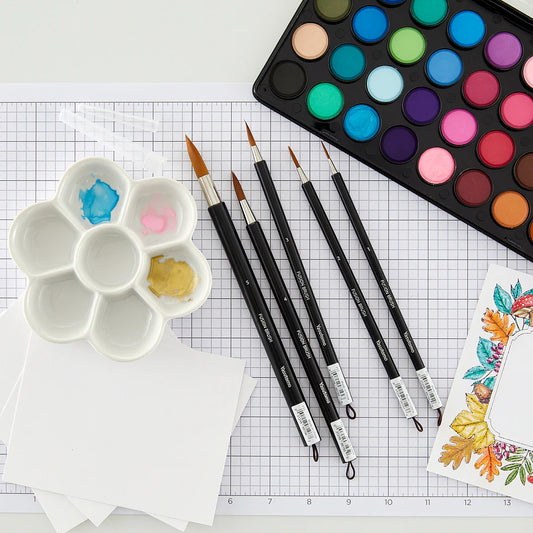 Yasutomo paintbrushes, a water color palette, and a floral design on grid paper.