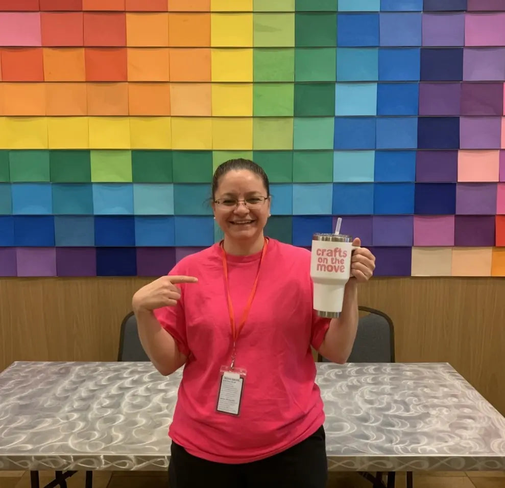 Andrea in pink shirt holding a cup with a colorful wall in the background