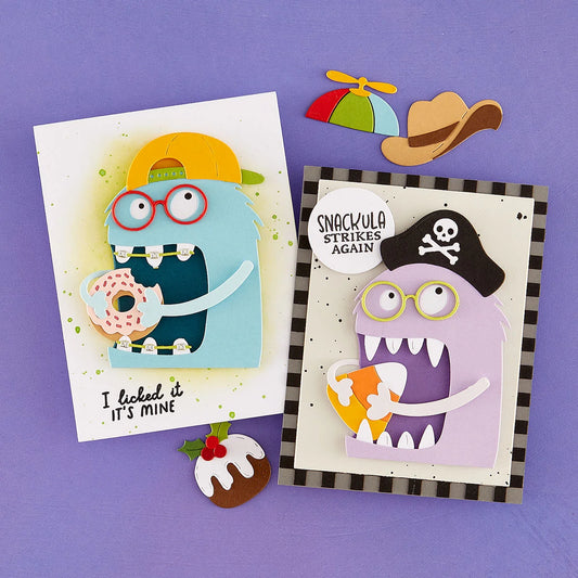 Two handmade layered paper cards displayed on a purple background, each featuring a cartoon monster with glasses and a speech bubble. One card shows a blue monster eating a donut and reads 'I licked it IT'S MINE.