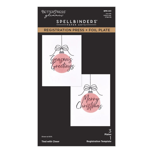 Better Press Glimmer Spellbinders Paper Arts Registration Press and Foil Plate package, featuring two sample holiday cards with pink ornament graphics and black text on a black card backing.