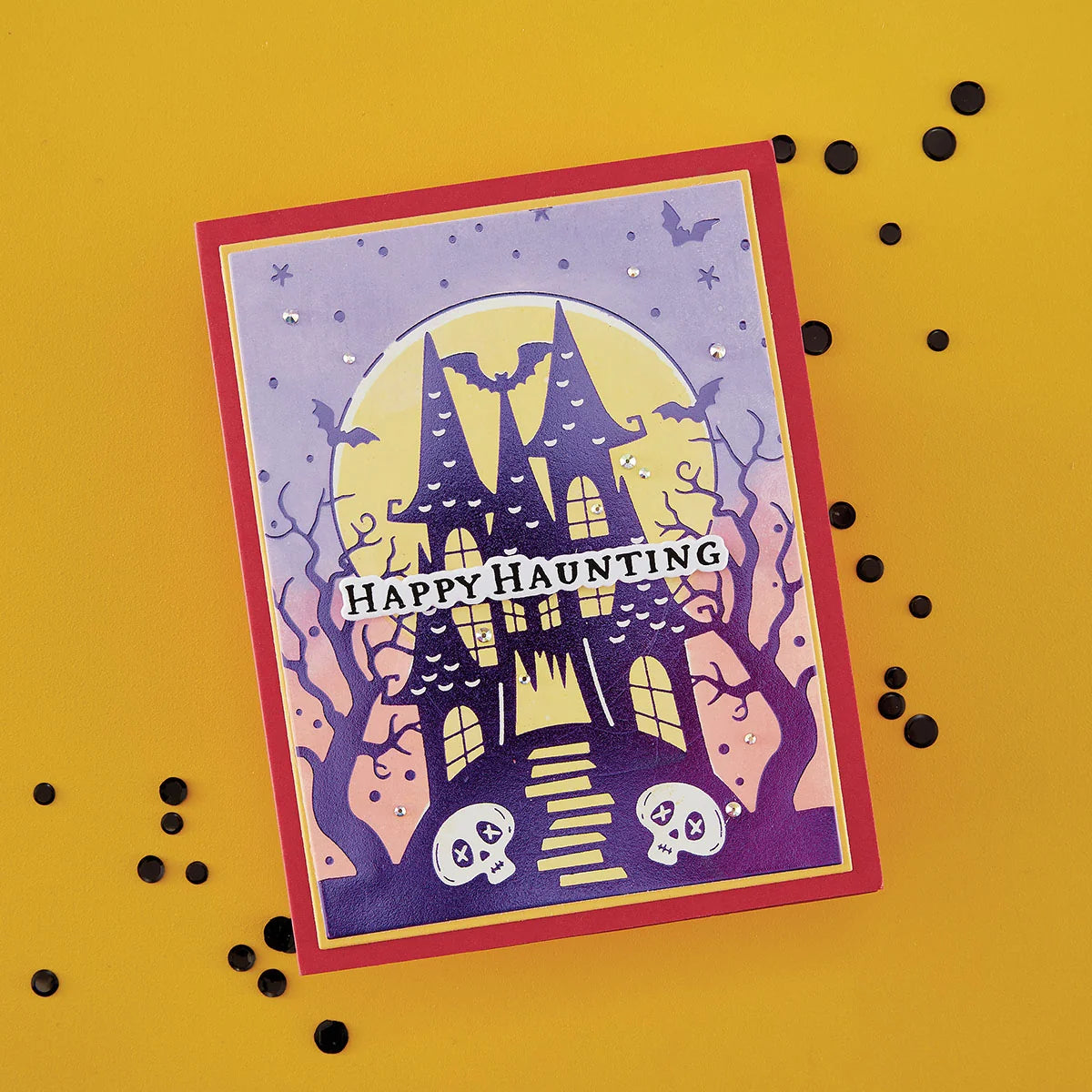 A Halloween-themed greeting card featuring a haunted house, bats, skulls, and the words 'Happy Haunting' on a yellow background with scattered black confetti.