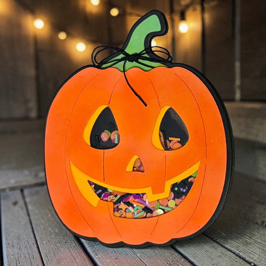 An orange jack-o'-lantern Halloween decoration filled with colorful candy, displayed on a wooden deck with warm string lights in the background.