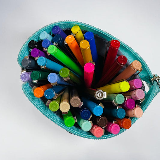 A teal zippered pencil pouch filled with a variety of colored pencils arranged in a radial pattern, photographed from directly above on a light gray background.