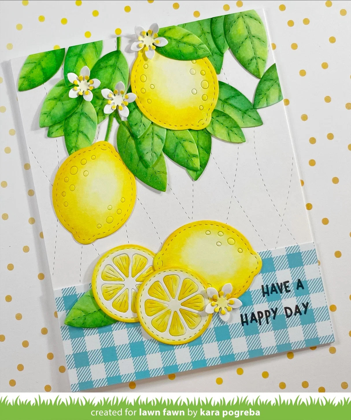A handmade greeting card featuring watercolor-style lemons, green leaves, small white flowers, and a blue-and-white gingham border with the text 'HAVE A HAPPY DAY'. The card is photographed on a white background with gold polka dots.