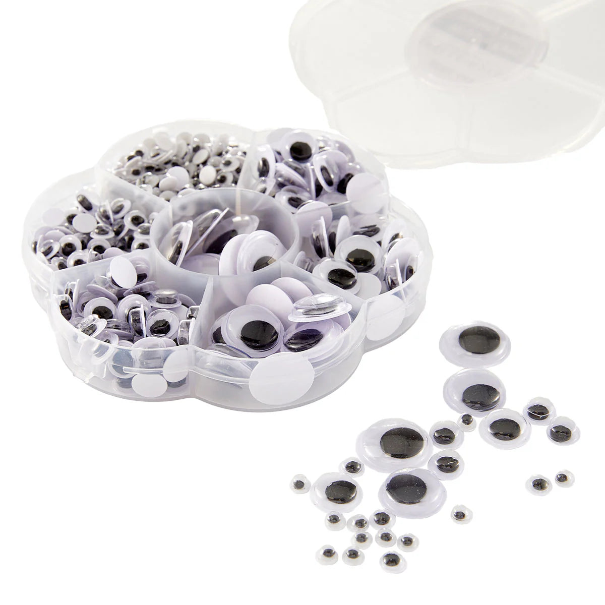 A clear plastic compartment organizer filled with white and black plastic googly eyes, with several loose googly eyes scattered on a white background. A translucent lid is partially visible at the top right.