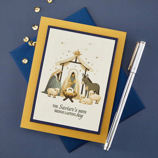 gold and blue card with a nativity scene in the center with a silver pen and gold sequins