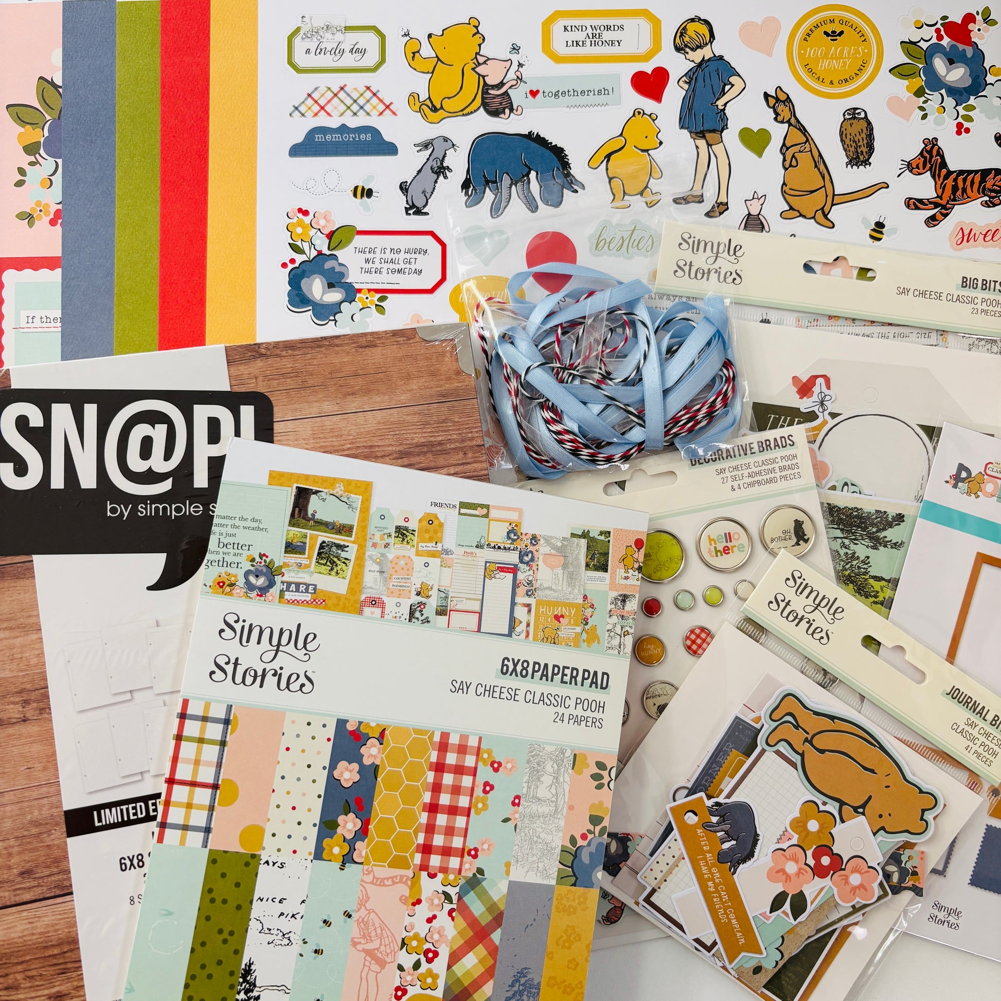 Scrapbooking supplies including paper pads, stickers, and ribbons on a wooden surface with 'Simple Stories' branding.