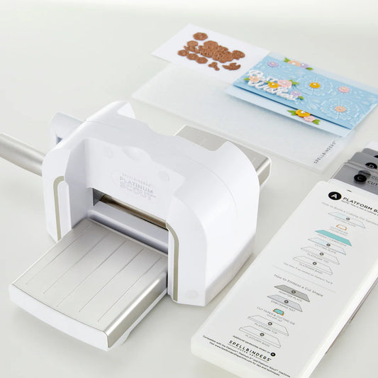 Spellbinders White die cutting machine on a white surface with printed cards and cutting plates.