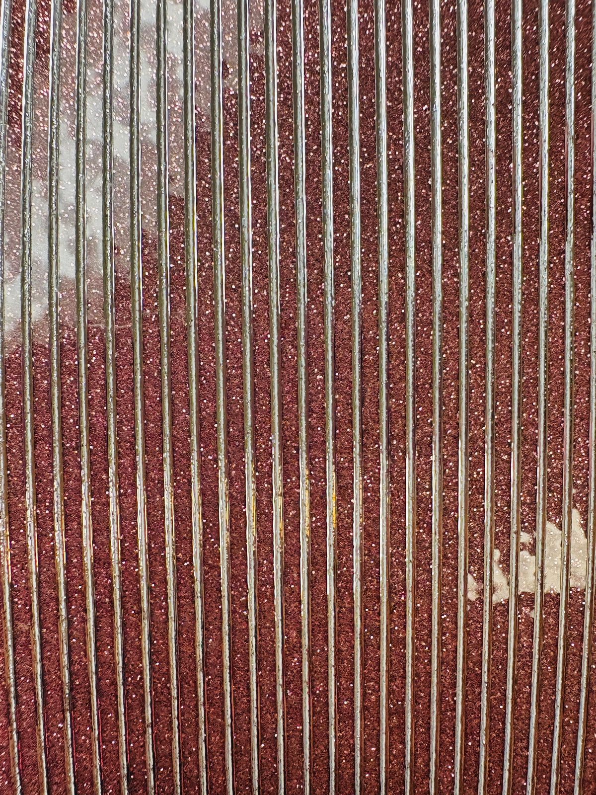 Pink glittered sticker strips surface with vertical lines and thin silver color.
