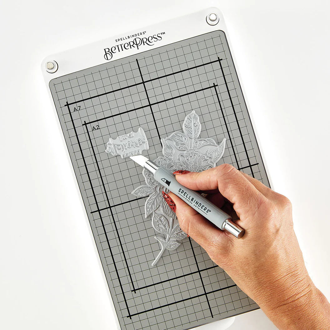 Hand using a die-cutting tool on a grid cutting mat with Spellbinders branding.