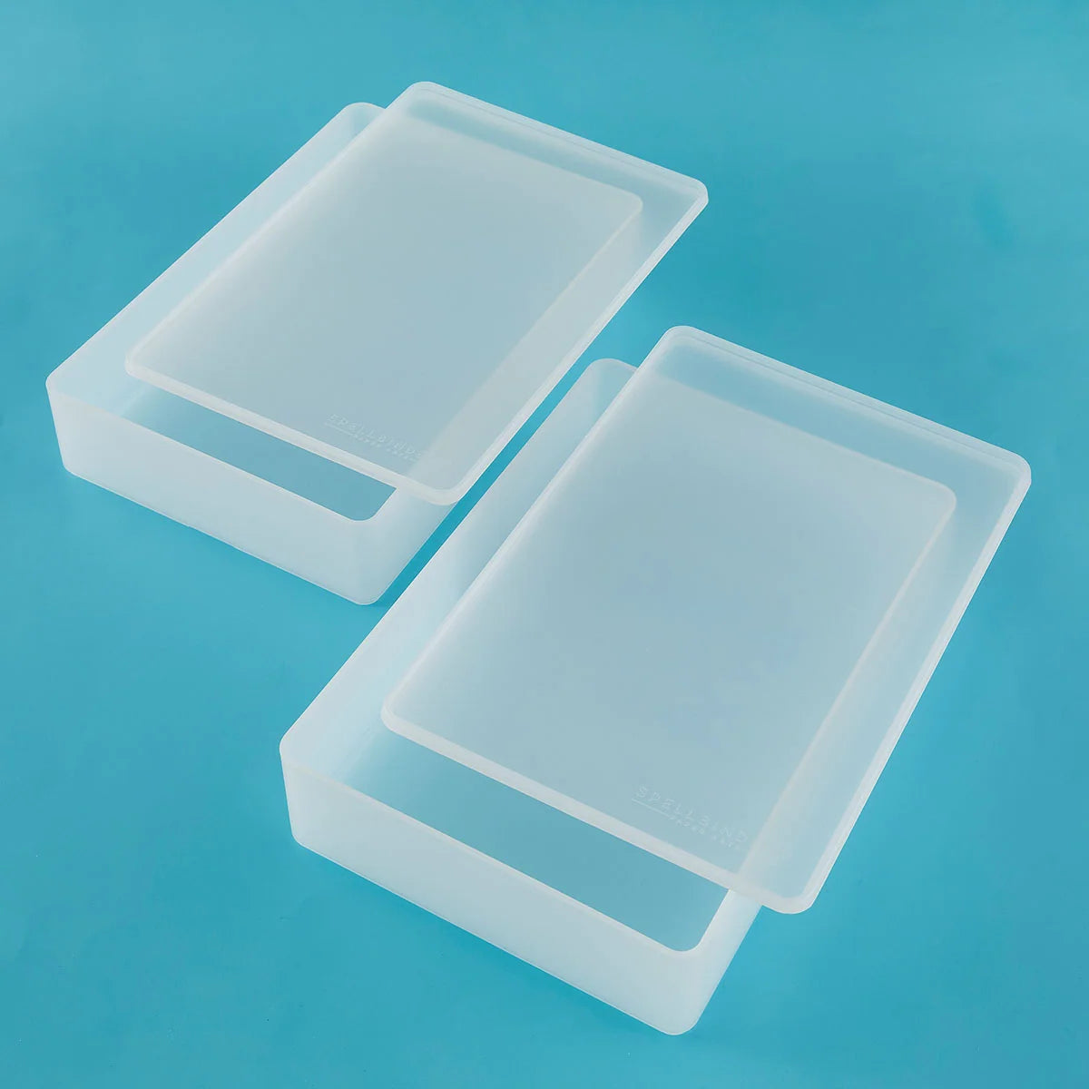 Two translucent white silicone mold trays with rectangular shapes, displayed on a solid blue background.