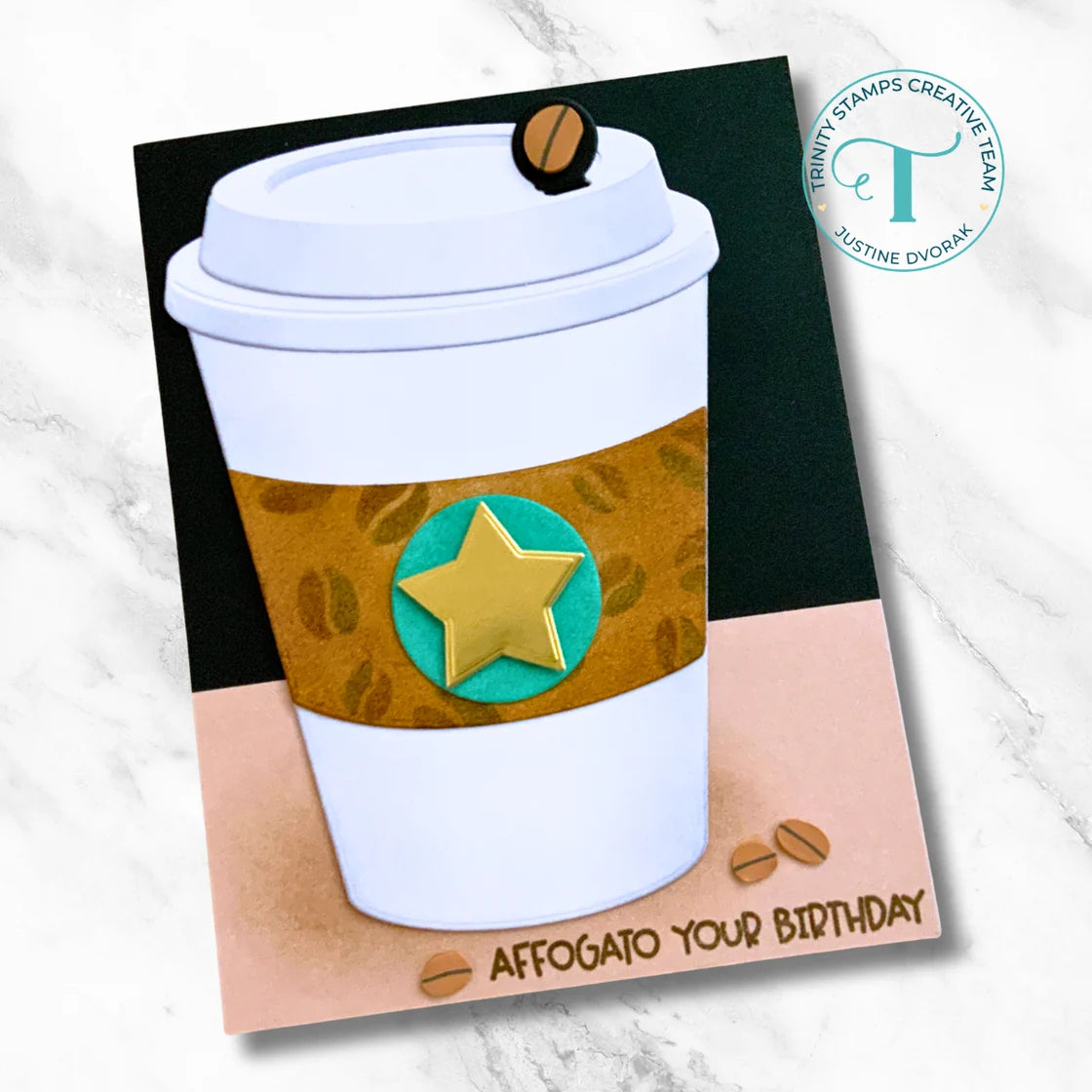 Trinity stamps logo and a card with a hot paper coffee cup with a gold star for decorations on a marble background