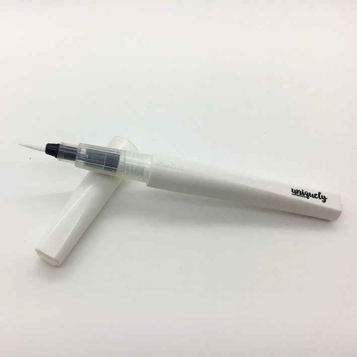 A white water sparkle brush pen with a clear cap and a black fine tip, shown with its matching white cap on a plain white background. The brand name 'uniquely' is printed in black on the barrel.
