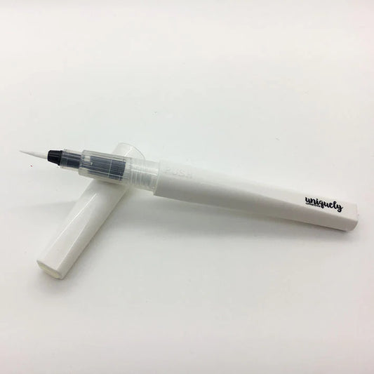 A white water sparkle brush pen with a clear cap and a black fine tip, shown with its matching white cap on a plain white background. The brand name 'uniquely' is printed in black on the barrel.